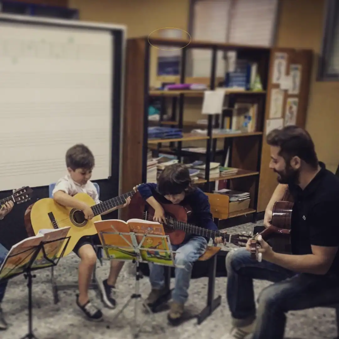 Estudiante tocando guitarra en clase de música con profesor en aula escolar.